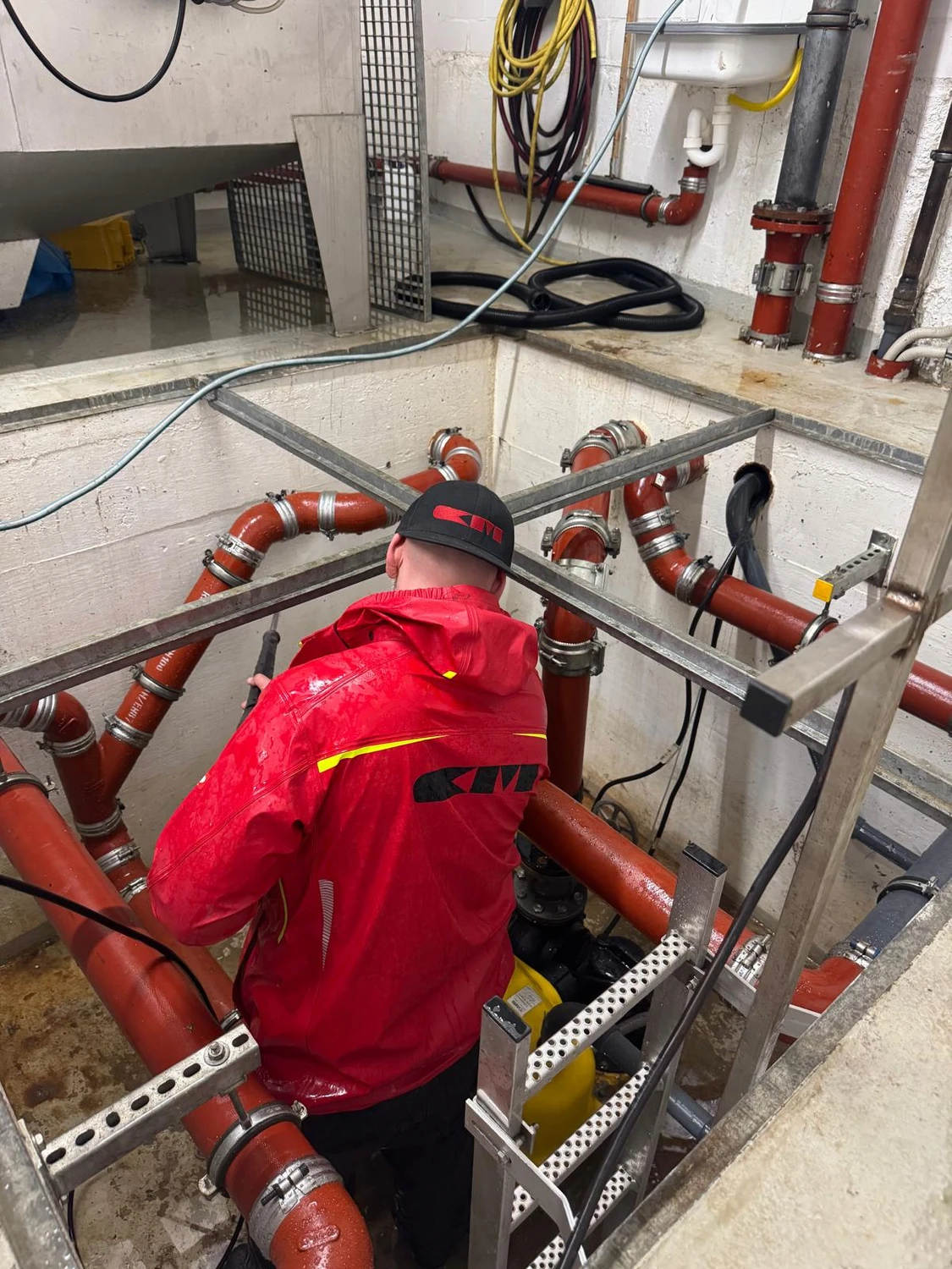 Christoph Mielke - Hausmeister Service & Graffitientfernung - Die Person trägt eine Regenjacke aus Aquaproof Vision-Stoff in Rot mit schwarzem KME-Logo.
